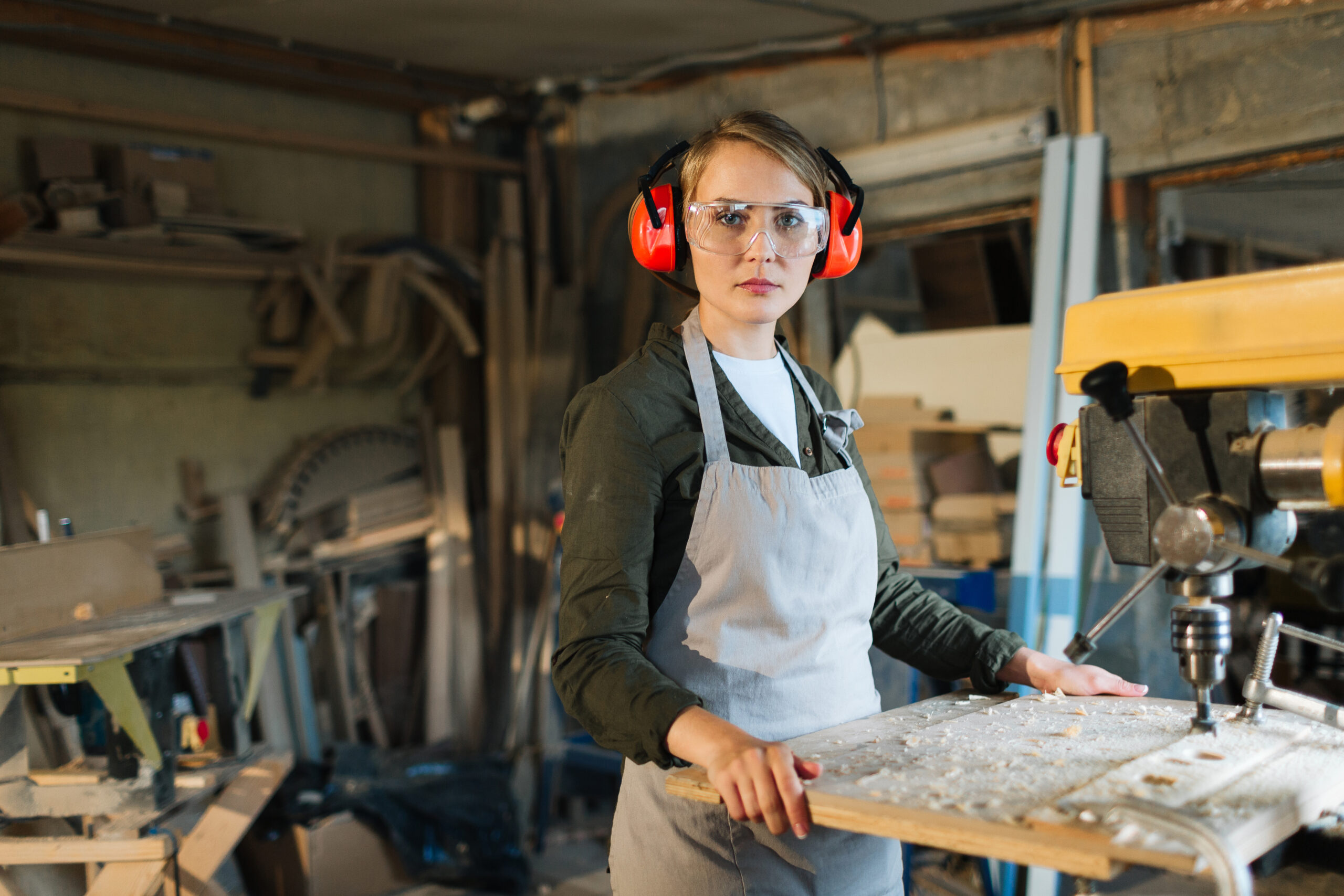 Beautiful drill press operator in eye and ear protectors posing for photography with serious look while distracted from work, waist-up portrait