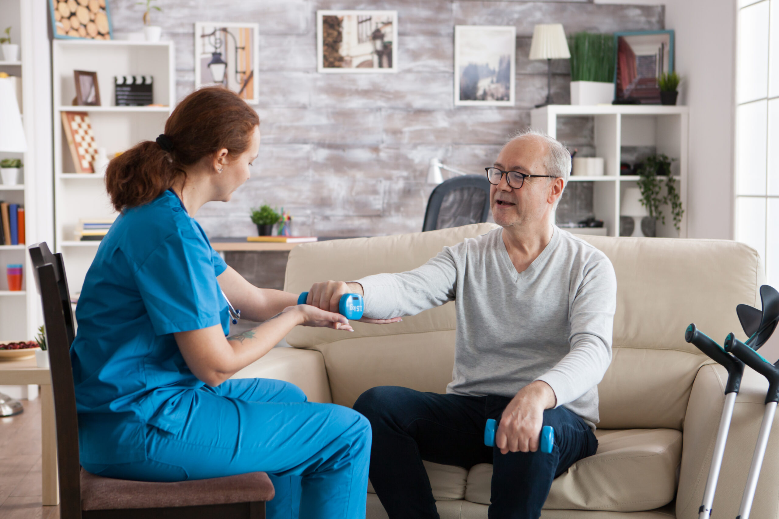 Senior man in nursing home with dumbbells doing physiotherapy with help from nurse.